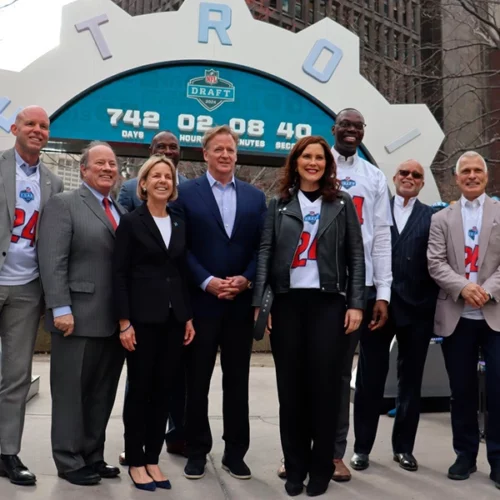 Group of officials posing in front of the NFL Draft countdown clock at 742 days in downtown Detroit