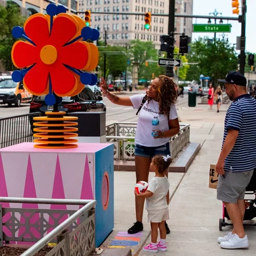 Family interacting with large flower sculpture in Bedrock streetscape
